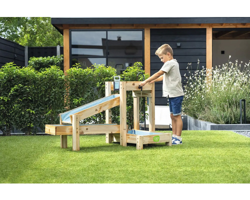 Kind spielt im Garten mit einer hölzernen Wasserbahn mit mehreren Ebenen und Auffangbecken auf einer Rasenfläche vor einem modernen Gartenhaus.