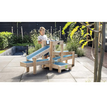 Ein Kind spielt im Garten mit einer mehrstufigen Wasserbahn aus Holz mit blauen Kunststoffrinnen auf einer gepflasterten Terrasse.