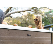 Außenansicht eines MSpa Whirlpools mit Paneelen in Holzoptik und Personen im Garten.