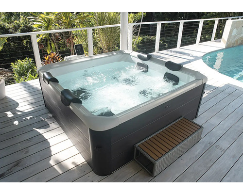 Außenwhirlpool mit dunkelgrauer Verkleidung und weißer Innenschale, Nackenkissen und sprudelndem Wasser auf einer Holzterrasse.