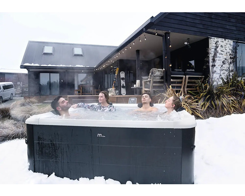 Vier Personen entspannen in einem MSpa Whirlpool im Freien inmitten einer Schneelandschaft vor einem modernen Holzhaus.