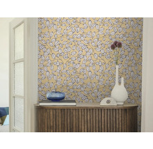Wohnraum mit gemusterter Blättertapete, einem Sideboard aus Holz, einer weißen Vase und einer blauen Glasschale.