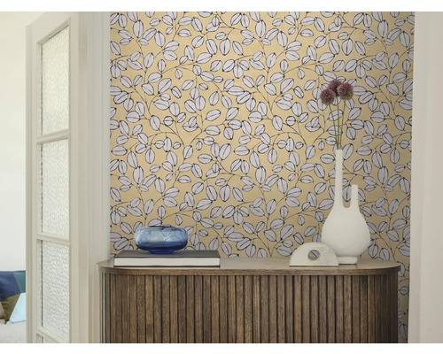 Wohnraum mit gemusterter Blättertapete, einem Sideboard aus Holz, einer weißen Vase und einer blauen Glasschale.