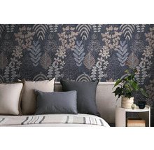 Vliestapete mit botanischem Blättermuster in Dunkelblau und Grau hinter einem Bett mit Kissen und einer Zimmerpflanze auf einem Beistelltisch.