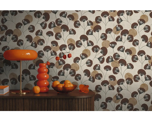 Vliestapete mit Blattmuster in Braun und Beige hinter einem Sideboard mit orangefarbener Lampe und Vase im Retro-Stil.