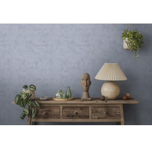 Rustikales Sideboard aus Holz vor strukturierter blau-grauer Wand mit Tischlampe, Steinskulptur, Glasflaschen und Zimmerpflanzen.