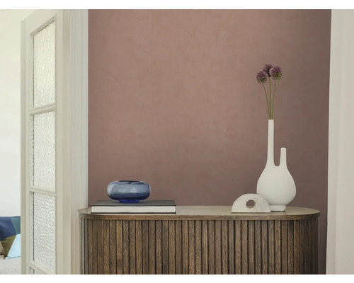Strukturierte Vliestapete in Altrosa auf einer Wand hinter einem Holzsideboard mit Lamellen, einer weißen Vase und einer blauen Glasschale.