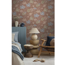 Vliestapete mit floralem Muster in Terracotta, Blau und Grün in einem gemütlich eingerichteten Raum mit Holzmöbeln und Textilien.
