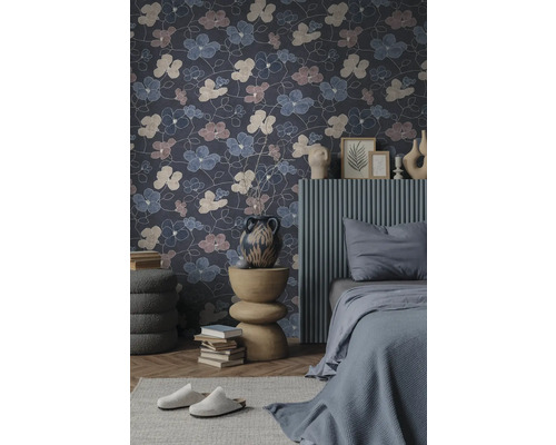 Vliestapete mit großflächigem Blumenmuster in einem modern eingerichteten Schlafzimmer mit grauem Bett und dekorativem Beistelltisch.