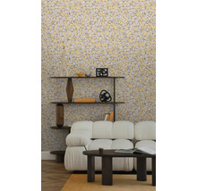 Vliestapete mit gelbem Blättermuster im hellen Wohnzimmer mit weißem Sofa, dunklem Couchtisch und Holzregal auf Parkettboden.