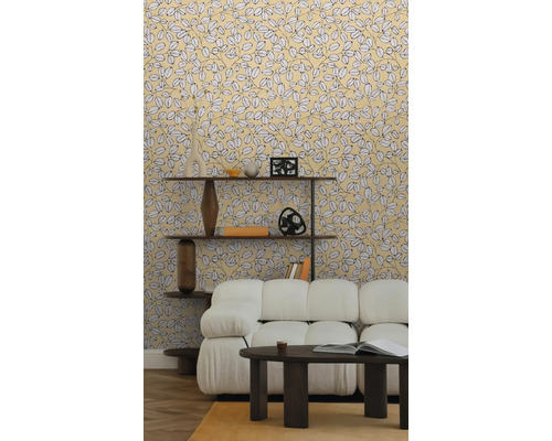 Vliestapete mit gelbem Blättermuster im hellen Wohnzimmer mit weißem Sofa, dunklem Couchtisch und Holzregal auf Parkettboden.