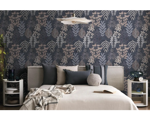 Schlafzimmer mit botanisch gemusterter Tapete mit verschiedenen Blattdesigns. Davor steht ein Bett mit hellem Kopfteil und dekorativen Kissen.