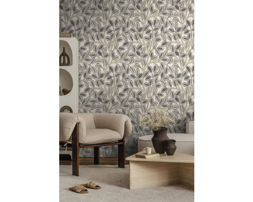 Modernes Wohnzimmer mit Vliestapete mit botanischem Blattmuster in Grau und Beige, hellem Sessel, Holztisch und weißem Regal.