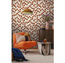 Wohnzimmer mit Mustertapete mit stilisierten Blättern in Terracotta und Grün. Mit orangefarbenem Cordsessel, einer Holzkommode und einem Beistelltisch.