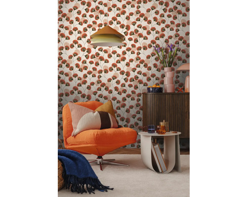 Wohnzimmer mit Mustertapete mit stilisierten Blättern in Terracotta und Grün. Mit orangefarbenem Cordsessel, einer Holzkommode und einem Beistelltisch.