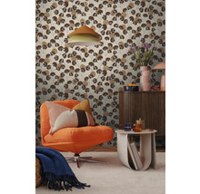 Wohnzimmer mit einer Mustertapete, die stilisierte braune Blätter zeigt, kombiniert mit einem orangefarbenen Sessel und einem hölzernen Sideboard.