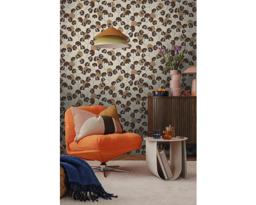 Wohnzimmer mit einer Mustertapete, die stilisierte braune Blätter zeigt, kombiniert mit einem orangefarbenen Sessel und einem hölzernen Sideboard.