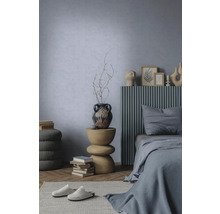 Modernes Schlafzimmer mit hellblau strukturierter Wand, Bett mit grauem Lamellen-Kopfteil und skulpturalem Beistelltisch aus Holz.