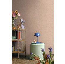 Modernes Wohnzimmer mit hellem Holzregal, farbenfrohen Dekorationsobjekten, grünem Polsterhocker und einer blauen Tischleuchte vor einer pfirsichfarbenen Wand.