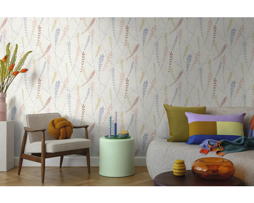 Vliestapete mit filigranem Blättermuster in einem hellen Wohnzimmer mit modernem Sessel, Sofa und Beistelltisch.
