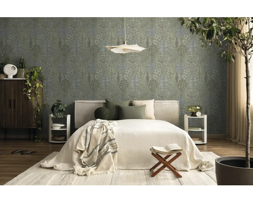 Schlafzimmer mit Vliestapete mit botanischem Blattmuster in Grün und Blau, helles Bett, Holzmöbel und Zimmerpflanzen.