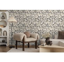 Vliestapete mit stilisiertem Blättermuster in einem modern eingerichteten Wohnzimmer mit Sessel, Stehlampe und Regal.
