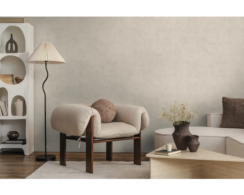 Modernes Wohnzimmer mit hellbeiger Wandfarbe in Betonoptik, hellem Sessel, Stehlampe und weißem Design-Regal auf Holzboden.