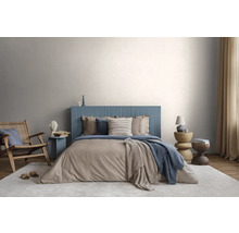 Modernes Schlafzimmer mit blauem, geriffeltem Kopfteil, beiger Bettwäsche, Holzstuhl und hellem Teppich vor einer lichtgrauen Wand.