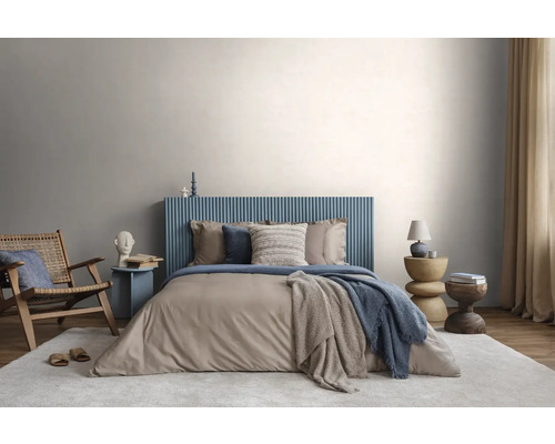 Modernes Schlafzimmer mit blauem, geriffeltem Kopfteil, beiger Bettwäsche, Holzstuhl und hellem Teppich vor einer lichtgrauen Wand.