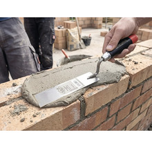 Hand trägt mit einer Maurerkelle Mörtel auf eine Ziegelwand auf einer Baustelle auf.