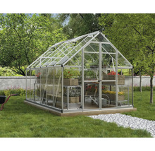 Großes Gewächshaus aus Aluminium mit Glaswänden und Dachfenstern in einem gepflegten Garten mit Pflanzen und Kiesweg.