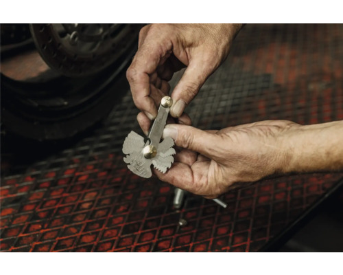 Eine Person hält eine Gewindelehre aus Metall in den Händen, um die Steigung eines Gewindes zu bestimmen.