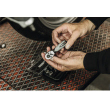 Hände halten eine WGB Bit-Ratsche über einer Werkbank in einer Werkstatt beim Schrauben an einem Motorrad.
