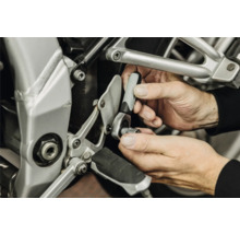 Hände benutzen eine kleine Umschaltknarre mit Steckschlüsseleinsatz bei einer Reparatur an einem Motorrad.
