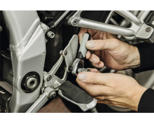 Hände benutzen eine kleine Umschaltknarre mit Steckschlüsseleinsatz bei einer Reparatur an einem Motorrad.