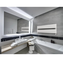 Modernes Badezimmer mit grauen Fliesen, großem beleuchtetem Spiegel, weißem Waschbecken, Badewanne und einem horizontalen Handtuchheizkörper.