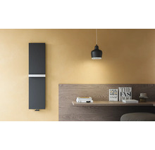 Moderner vertikaler Designheizkörper in Dunkelgrau mit weißem Handtuchhalter an einer gelben Wand neben einem Holztisch.