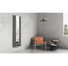 Vertikaler Designer-Heizkörper mit integriertem Ganzkörperspiegel in einem modern gestalteten Wohnraum mit Ledersessel und Sichtbetonwänden.