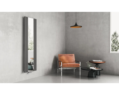 Vertikaler Designer-Heizkörper mit integriertem Ganzkörperspiegel in einem modern gestalteten Wohnraum mit Ledersessel und Sichtbetonwänden.