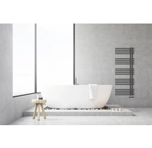 Modernes helles Badezimmer mit freistehender weißer Badewanne, anthrazitfarbenem Handtuchheizkörper an einer Wand in Betonoptik und Holzhocker.