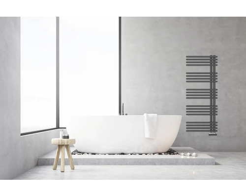 Modernes helles Badezimmer mit freistehender weißer Badewanne, anthrazitfarbenem Handtuchheizkörper an einer Wand in Betonoptik und Holzhocker.
