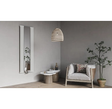 Vertikaler Design-Heizkörper mit integriertem Spiegel in einem hellen, modernen Wohnzimmer mit Sessel, Beistelltischen und einer Zimmerpflanze.