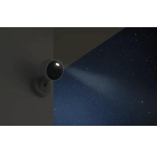 Überwachungskamera für den Außenbereich mit integriertem Scheinwerfer an einer Wand bei Nacht unter einem Sternenhimmel.