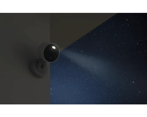 Überwachungskamera für den Außenbereich mit integriertem Scheinwerfer an einer Wand bei Nacht unter einem Sternenhimmel.