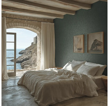 Schlafzimmer mit dunkelgrüner Strukturtapete, weißem Bett, Decke mit Holzbalken und einem Steinbogen mit Blick auf das Meer.