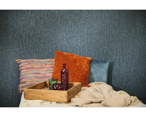 Strukturierte blaue Tapete in einer Raumszene mit dekorativen Kissen in Orange, Blau und Bunt, einem Holztablett und einer gestrickten Decke.