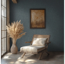 Rustikales Zimmer mit strukturierter Wand, Holzstuhl mit Rattangeflecht, Vase mit Pampasgras und gerahmtem Bild in hellem Tageslicht.