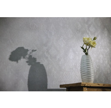Vliestapete mit dezentem Ornamentmuster und Struktur, davor eine Vase mit Rosen auf einer Holzoberfläche.