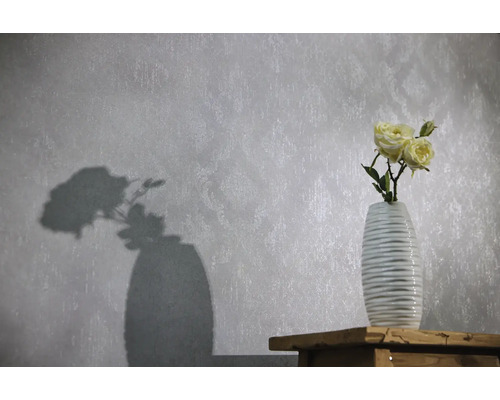 Vliestapete mit dezentem Ornamentmuster und Struktur, davor eine Vase mit Rosen auf einer Holzoberfläche.