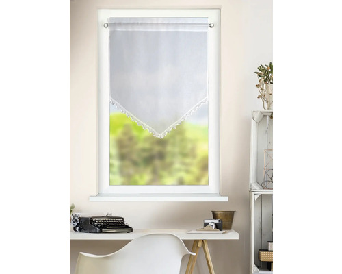 Weißer, transparenter Bistrovorhang mit spitz zulaufender Häkelspitze in einem hellen Zimmer über einem Schreibtisch mit Schreibmaschine.